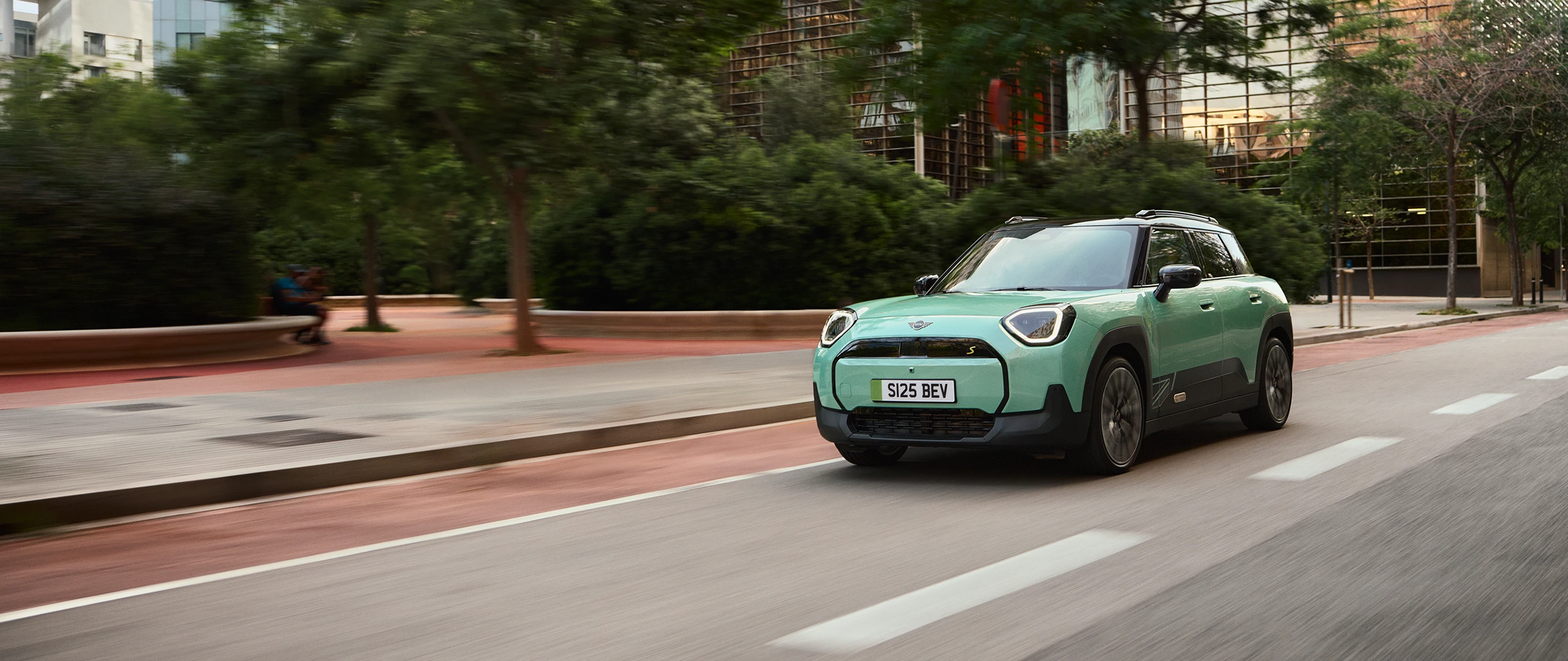All‑electric MINI Aceman in Rebel Green driving through a city street